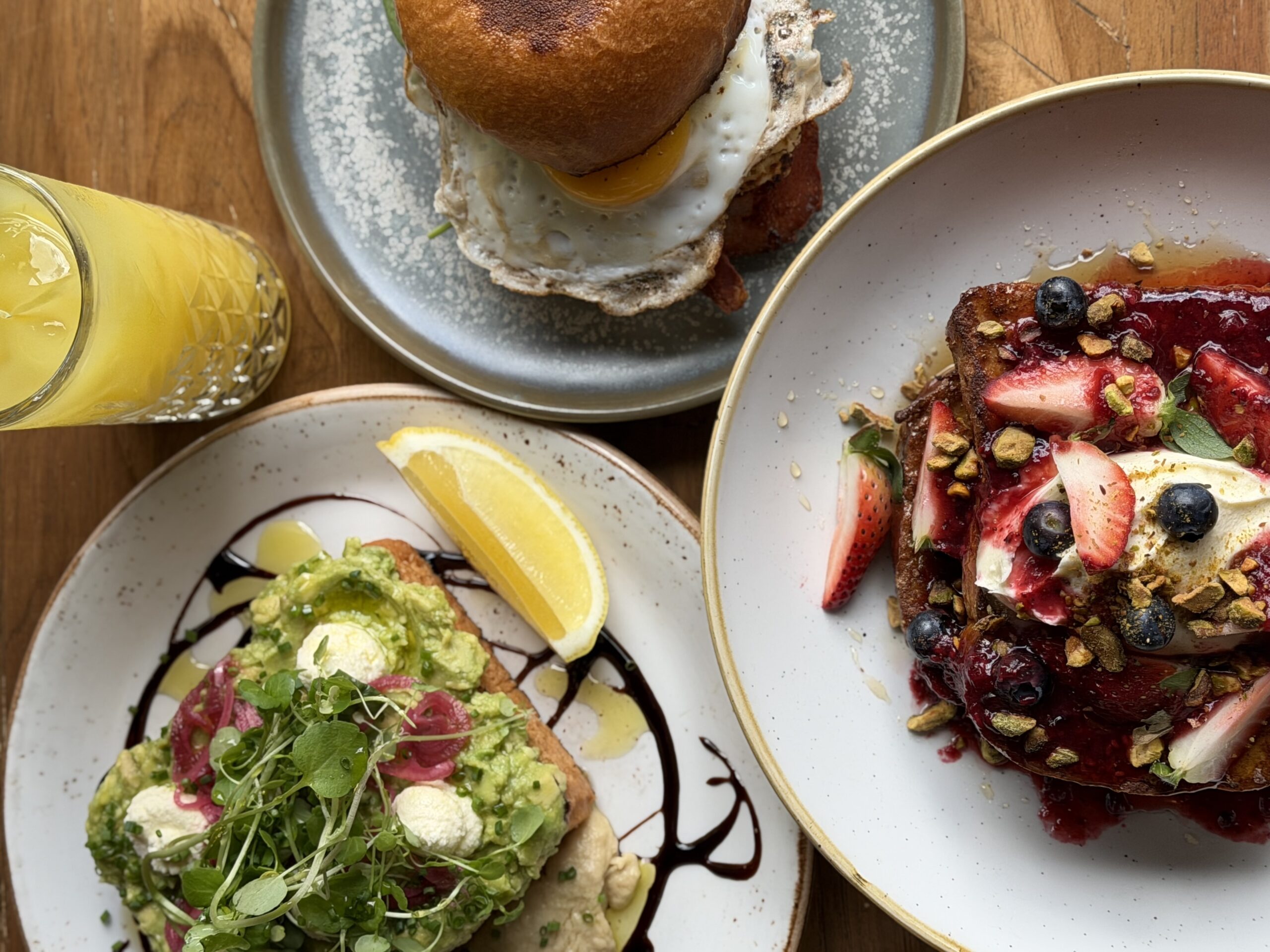 Breakfast table at Azure Mediterranean with avocado toast, french toast and a breakfast burger with a glass of orange juice.
